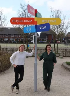 Martine (links) en Michelle (rechts) staan bij een wegwijzer met de tekst welkom in verschillende kleuren