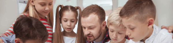 Een leraar met leerlingen aan bureau.