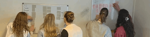 Vijf studenten die werken aan een project op een whiteboard.