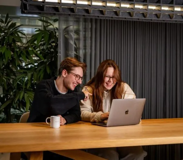 twee studenten zitten lachend achter een laptop