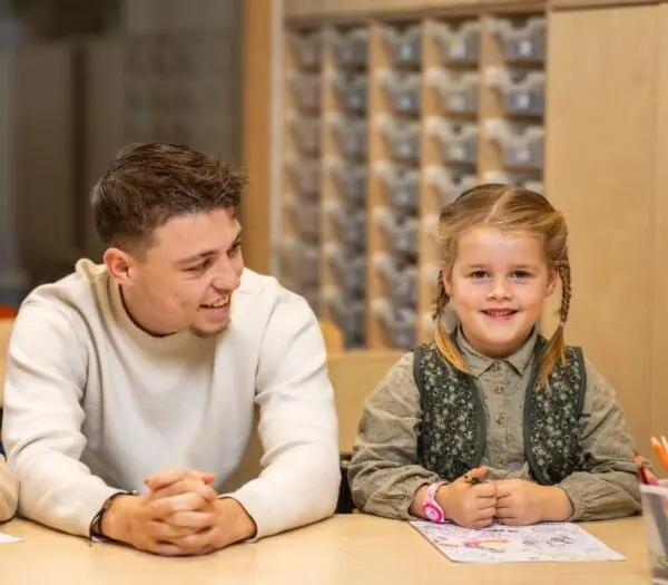 pabo student zit naast leerling, die in de camera kijkt