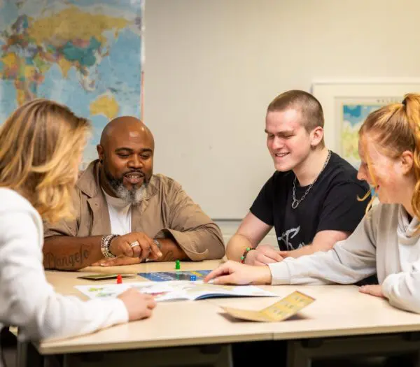 Studenten werken samen aan tafel onder begeleiding van docent