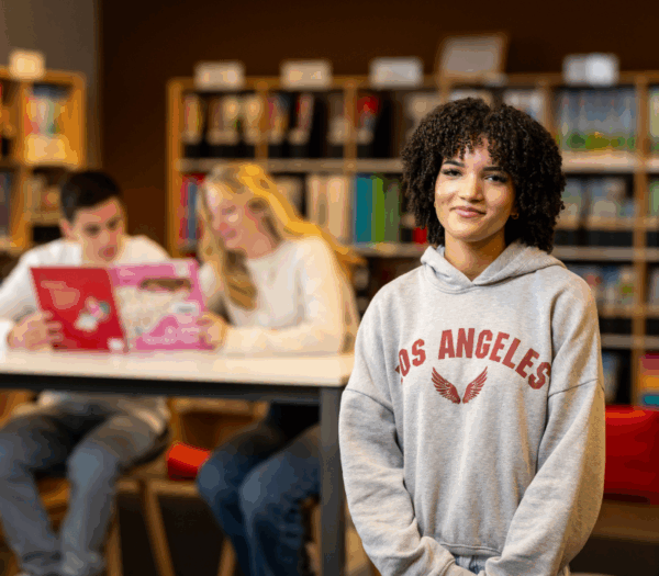 Student kijkt in de camera met in de achtergrond twee lezende studenten