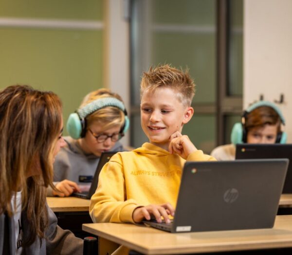 Docent kijkt naar kind achter de laptop