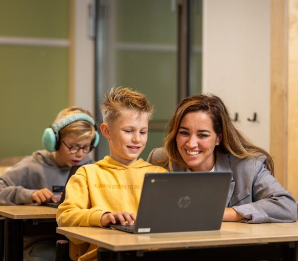 Docent helpt kind achter de laptop