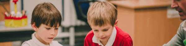 Twee leerlingen die samen met een leerkracht werken aan een opdracht.