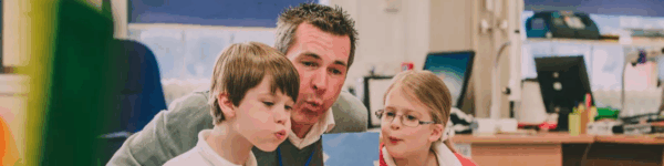 Leerkracht die met twee leerlingen een proefje doet.