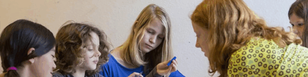 Een leerkracht die instructies geeft aan drie leerlingen.