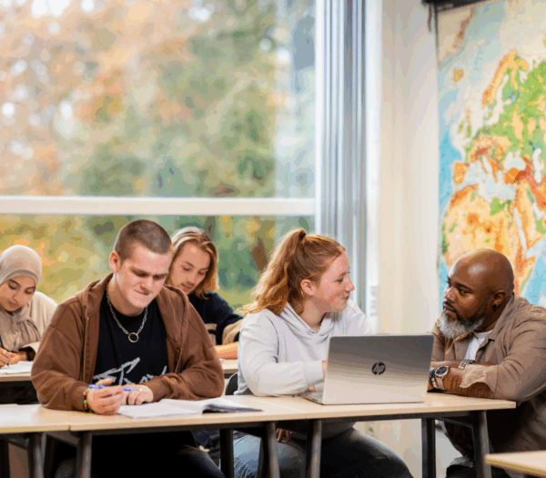 Studenten in klaslokaal aan het werk, 1 student overlegt met docent