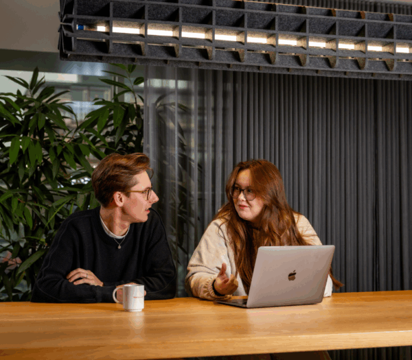 Twee studenten praten met elkaar achter een laptop