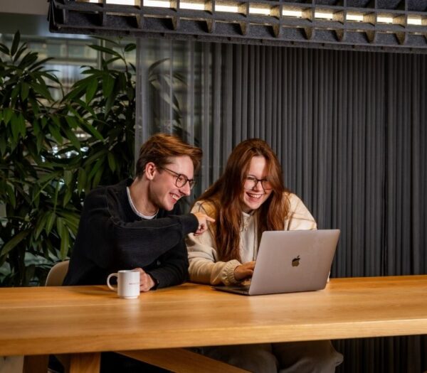 twee studenten zitten lachend achter een laptop