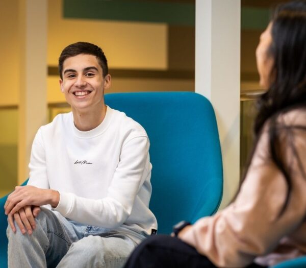 Jongen zit tegenover vrouw en lacht in de camera